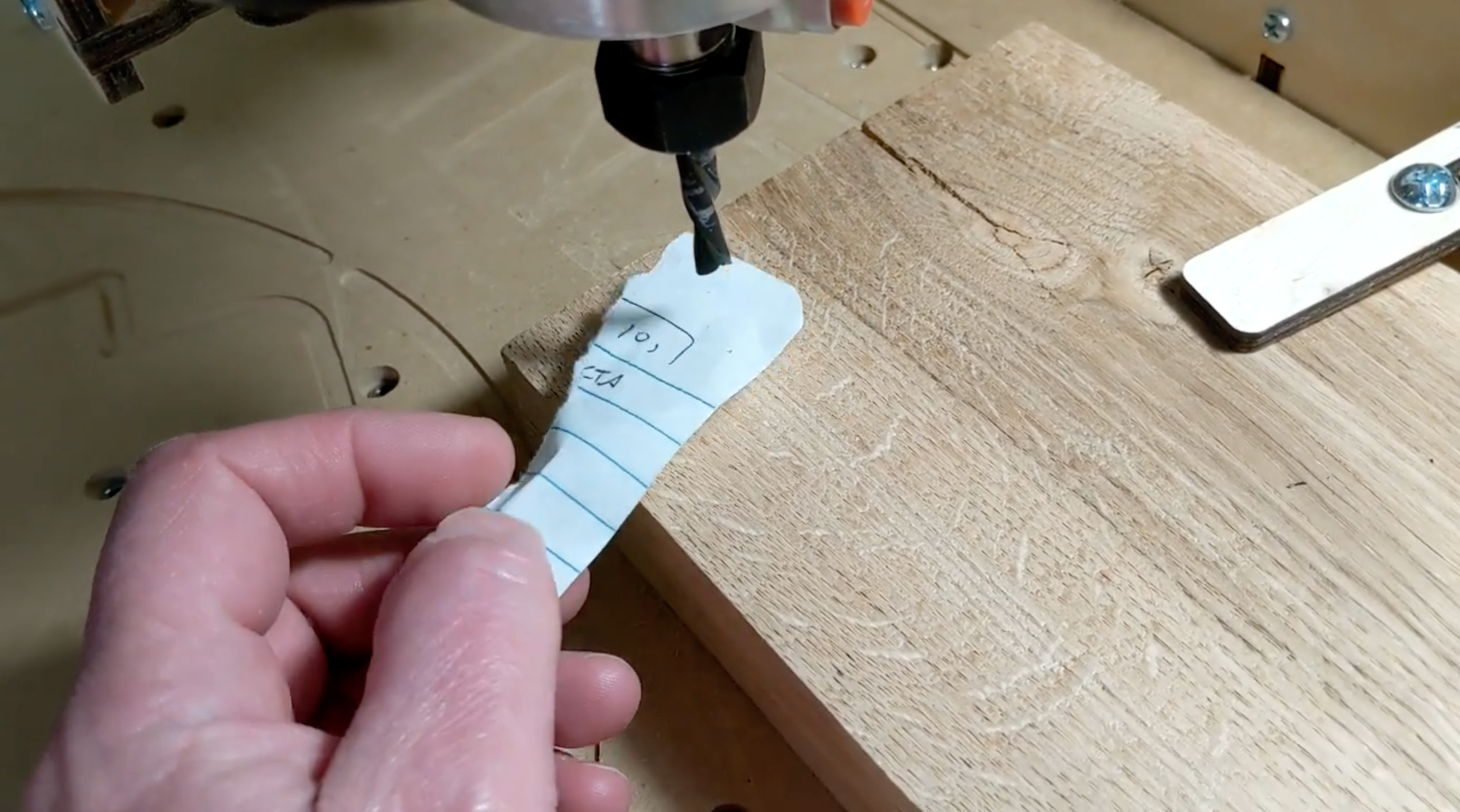 Man holds a piece of paper on a wood block under a drill on a CNC router